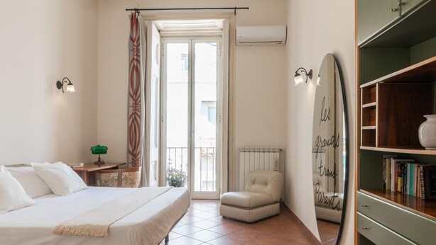 A bedroom with a bed, a chair, a radiator, a bookshelf, and a door leading to a balcony. - Maiorani Family Apartment nel Centro di Napoli (Naples)