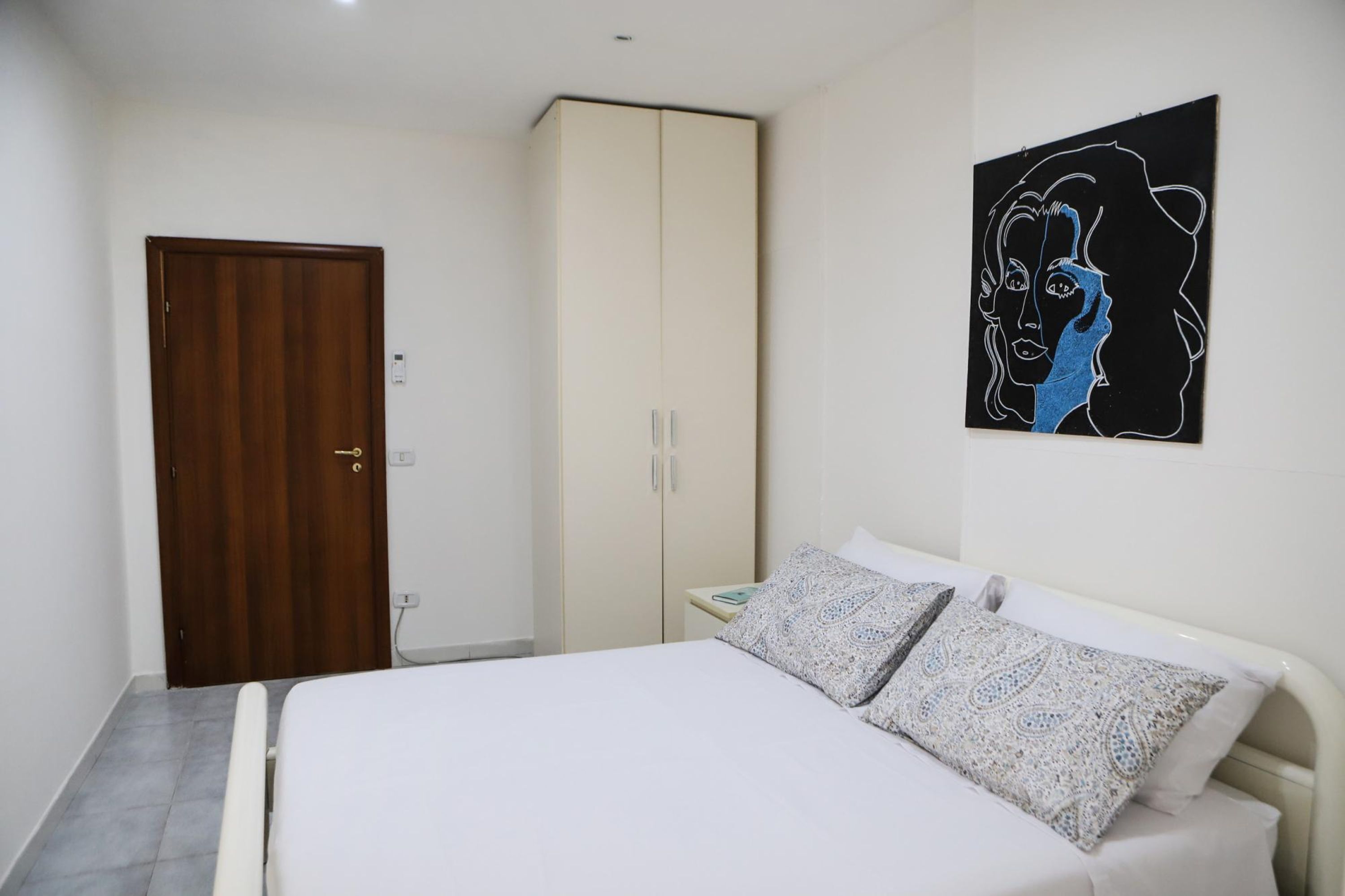 A bedroom with a bed, a wardrobe, and a wall-mounted artwork.