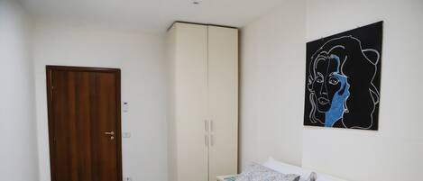 A bedroom with a bed, a wardrobe, and a wall-mounted artwork.