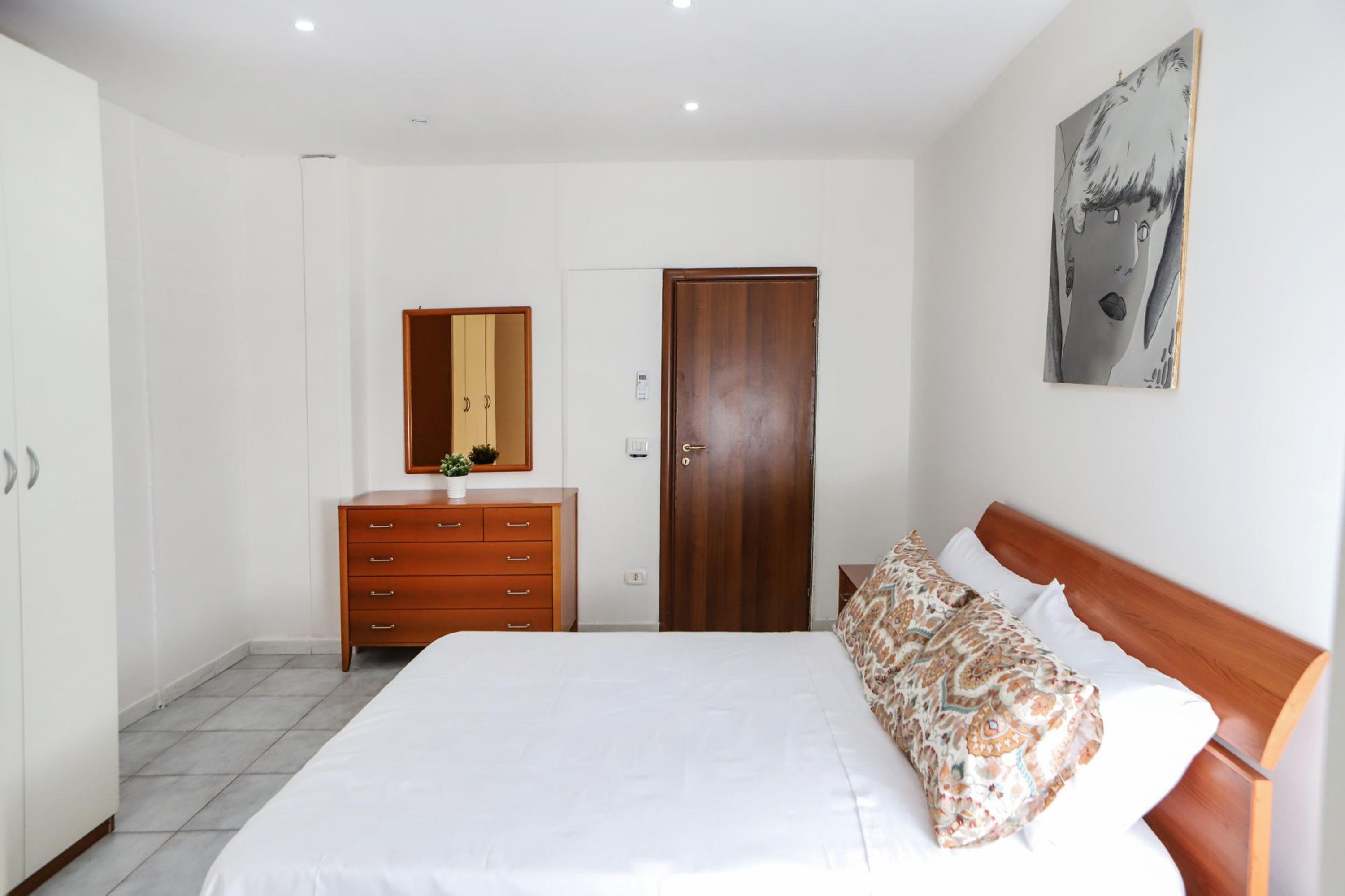 Une chambre à coucher avec un lit, une commode, une porte en bois et un miroir fixé au mur.