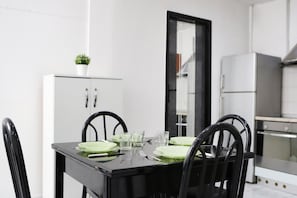 Una mesa de comedor con cuatro sillas, un armario blanco con puertas de vidrio y un refrigerador al fondo.