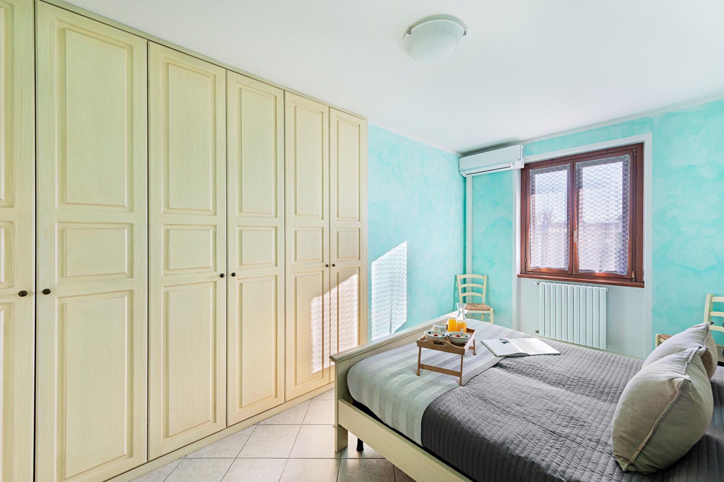 Un dormitorio con cama, armario, ventana y radiador.