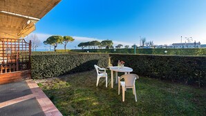 Area esterna con tavolo e sedie, un pergolato in legno e vista su alberi e edifici in lontananza.
