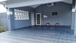 A covered outdoor area with a tiled floor, a decorative wall panel, a door, and two potted plants.