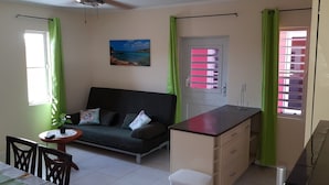 A compact living space with a sofa, a small dining table, a kitchenette, and a window with curtains.