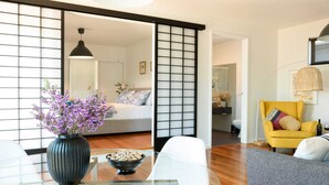 A modern living room with a sliding shoji screen, a sofa, a yellow armchair, and a glass coffee table with a vase of flowers. - Daydream Cottage (Daylesford)