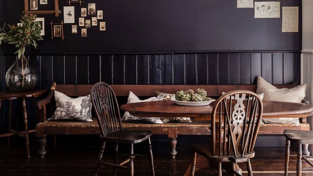 A dark-themed dining area with a wooden bench, chairs, and a table. - L'Papillon (Daylesford)