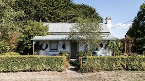 A white house with a grey roof, surrounded by greenery and trees. - L'Papillon (Daylesford)