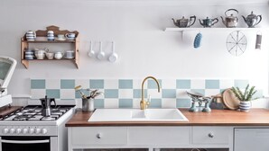 A kitchen with a white sink, wooden countertop, and a gas stove. There are shelves with kitchenware and a wall-mounted rack with teapots. - L'Papillon (Daylesford)