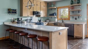 A kitchen with wooden cabinets, a large island with stools, a microwave, and a dishwasher. - Sleeps 20! Fire Pit, Hot Tub & Amazing Location! (Asheville)