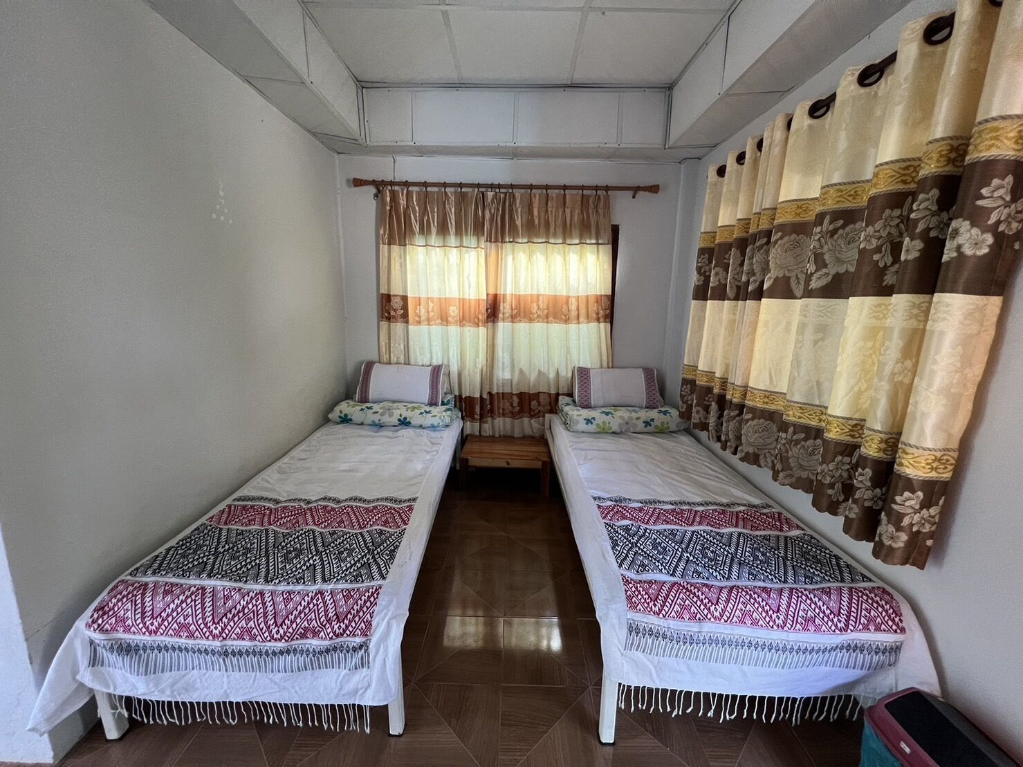 Une chambre avec deux lits simples, une fenêtre avec des rideaux et un mur décoré de motifs.