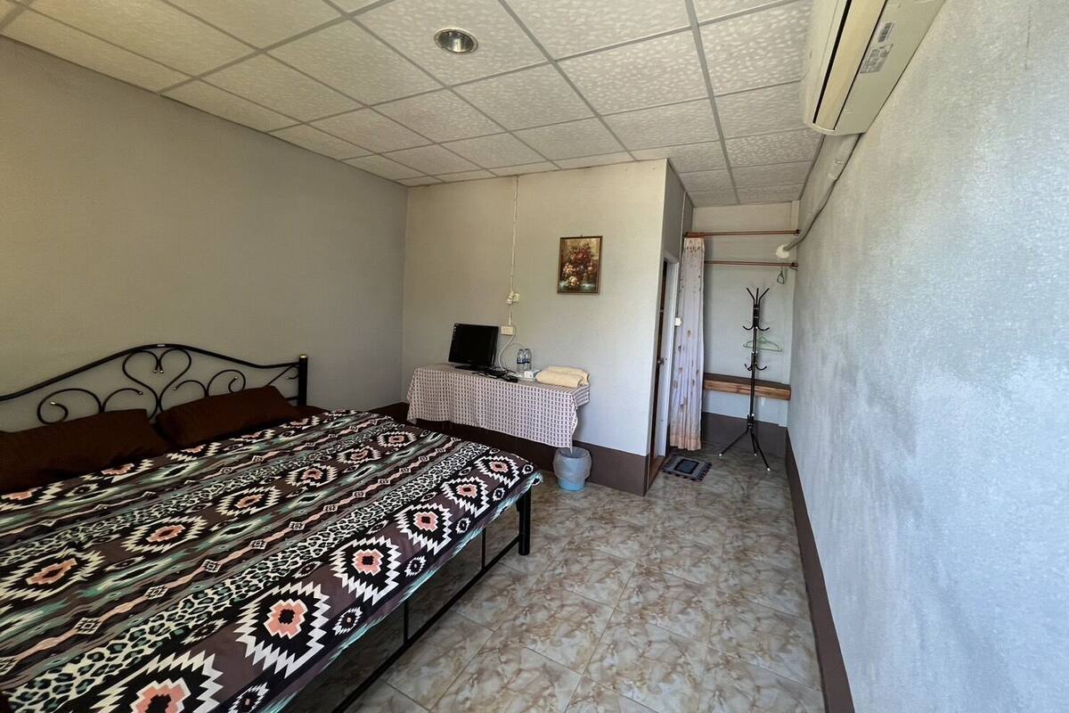 A bedroom with a bed, a desk with a computer, a coat rack, and a door leading to another room.