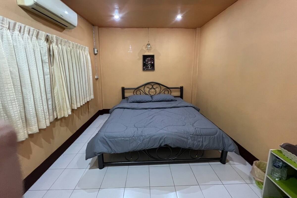A bedroom with a bed, curtains, an air conditioner, a small wall-mounted picture, and a tiled floor.