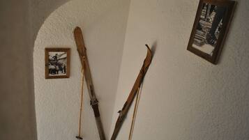 Une pièce avec un mur blanc à la texture particulière, un tableau encadré et deux paires de skis appuyés contre le mur.