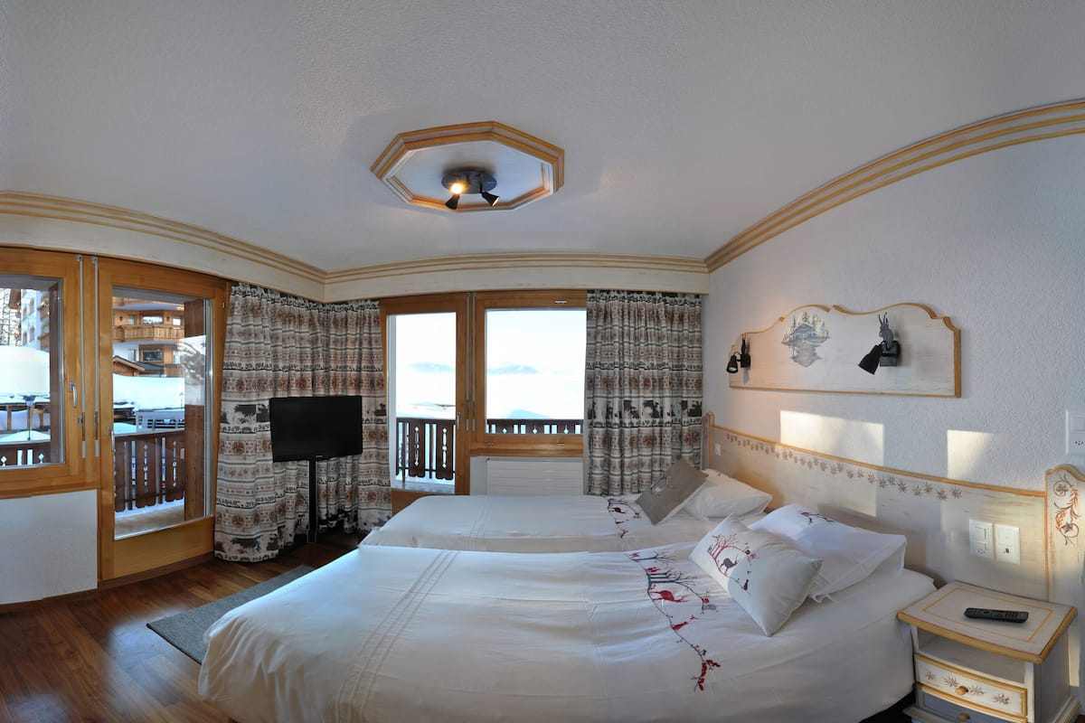 A hotel room with two beds, a TV, a balcony with a view, and a ceiling light fixture.