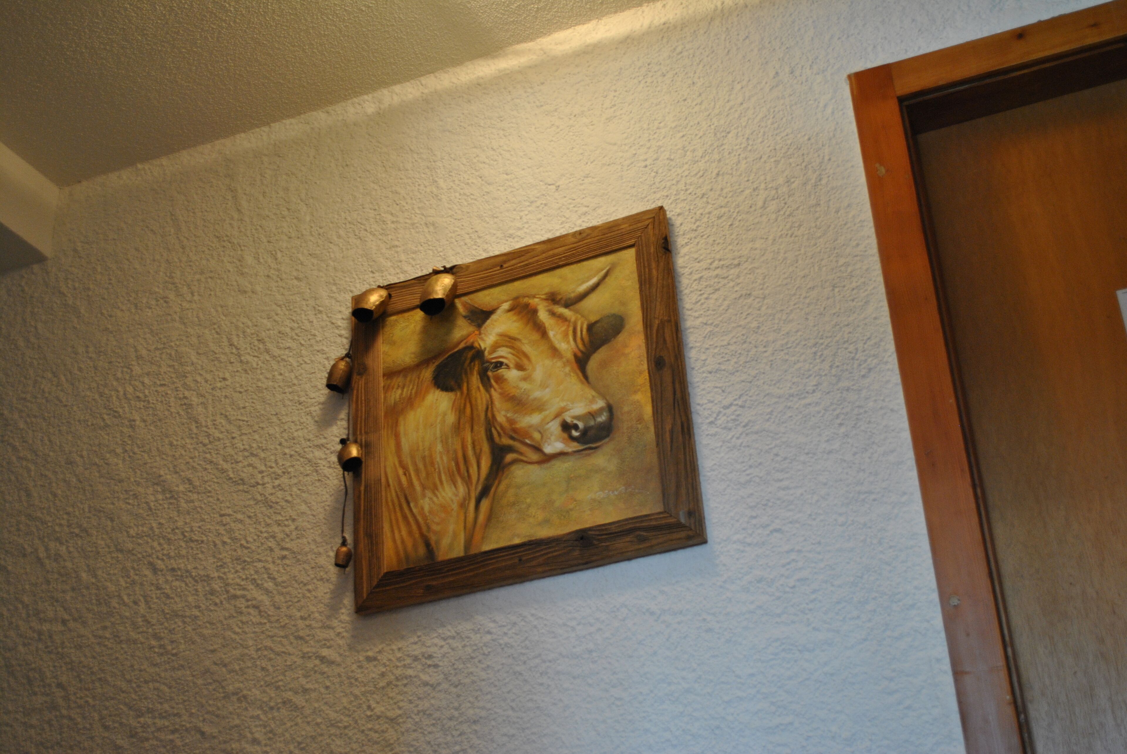 Kehyksiin asetettu maalaus, jossa on kuvattuna lehmä ja taustalla kuvioitu seinä.