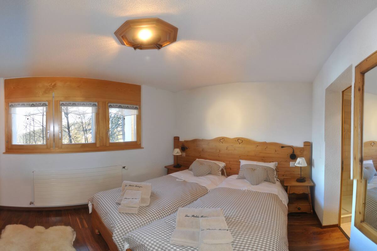 A bedroom with two beds, wooden headboards, a large window, and a ceiling light.