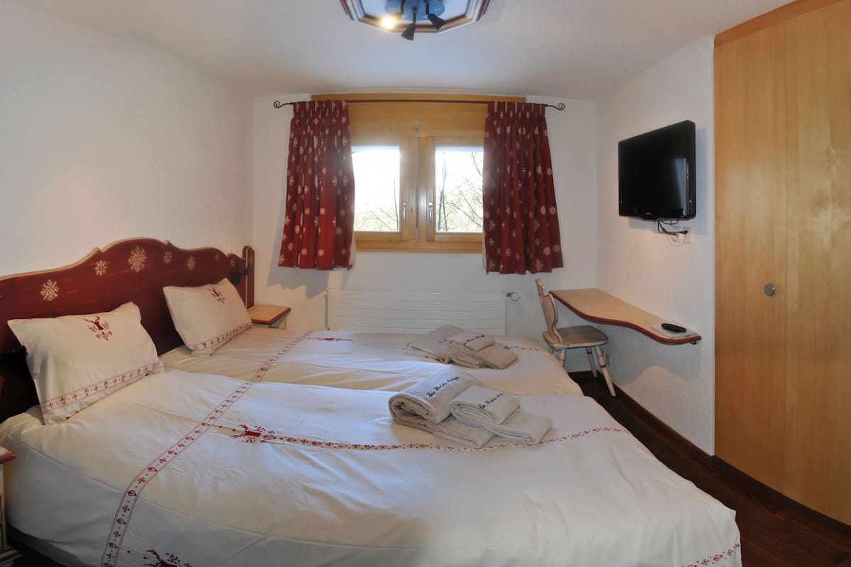 A hotel room with a large bed, a wooden headboard, a desk with a chair, a television, and a window with curtains.