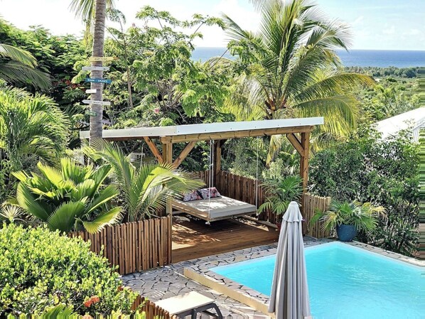 A poolside area with a wooden deck, a swing chair, and a covered seating area.