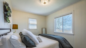 Ein Schlafzimmer mit Bett, Nachttischlampe, Fenster und einer an der Wand befestigten Pflanze.