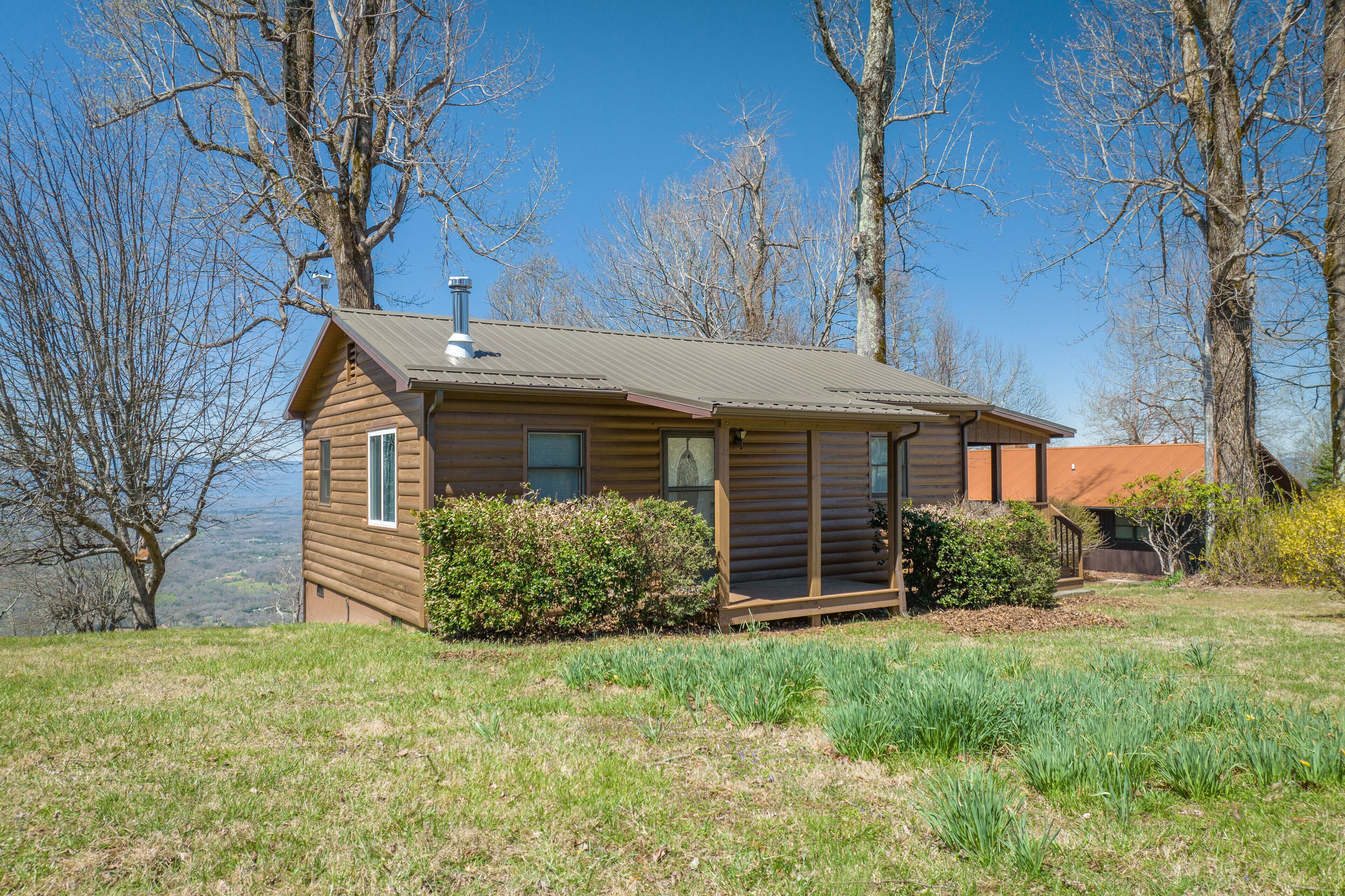 A small log cabin with a chimney, a porch, and a view of the surrounding landscape.
