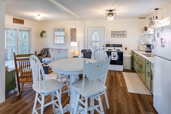 A cozy kitchen with a round table, white chairs, wooden cabinets, and a refrigerator.