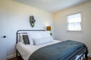 A neatly made bed with a grey blanket and white linens, a wall-mounted plant, and a window with blinds.