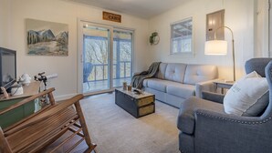 Ein Wohnzimmer mit einer Couch, einem Schaukelstuhl, einem Couchtisch und einer Lampe. An der Wand befindet sich ein Schild mit der Aufschrift 'CABIN'.