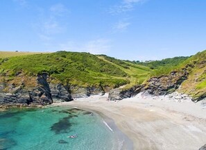 Een kustlandschap met een zandstrand, helder turquoise water en groene heuvels.