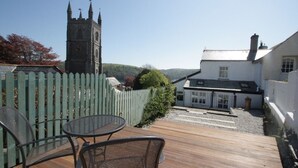A wooden deck with a table and chairs, a white building with a chimney, and a church tower in the background. - Private garden & central location  within 5 min walk of town (Fowey)