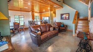 A spacious living area with a large brown leather sofa, a dining table with chairs, and a kitchen in the background. - Exquisite Hill Country Cottage-Giraffe and wildlife experiences (Lometa)