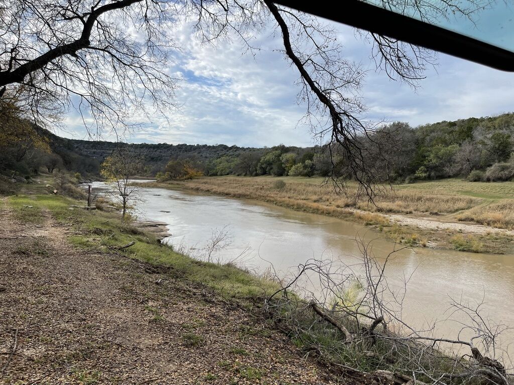 A river flowing through a natural landscape with trees and hills in the background.