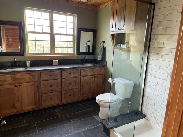 Une salle de bain avec un meuble-lavabo en bois, une cabine de douche en verre, des toilettes blanches et une fenêtre qui laisse entrer la lumière naturelle.