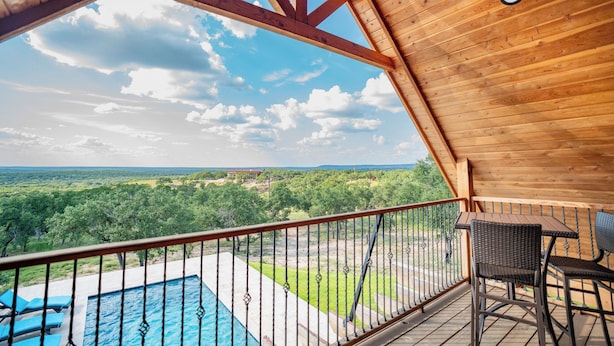 A wooden balcony with a pool and chairs overlooking a lush landscape. - Exquisite Hill Country Cottage-Giraffe and wildlife experiences (Lometa)