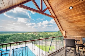 Un balcon en bois avec une piscine et des chaises, offrant une vue sur un paysage luxuriant.