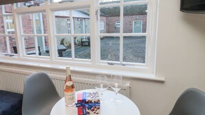 A table with a bottle of wine, glasses, and a gift box in a room with a view of brick buildings through large windows. - Silverbirch (Cornhill on Tweed)