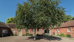 A traditional brick building with a gravel courtyard, a large tree, and a clear blue sky. - Silverbirch (Cornhill on Tweed)
