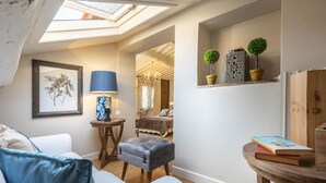 Una habitación acogedora con tragaluces, una cama, una lámpara azul, una mesita con libros y plantas decorativas.