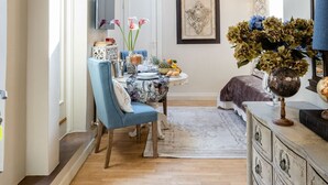 Un comedor con una mesa dispuesta para dos, una silla tapizada en azul y un aparador de estilo antiguo con varios cajones.