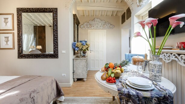 Una habitación con una cama, una mesa de comedor con platos, un jarrón con flores y un espejo en la pared.
