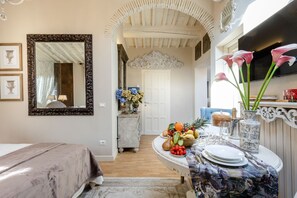 Une pièce comprenant un lit, une table à manger dressée avec des assiettes, un vase rempli de fleurs et un miroir accroché au mur.