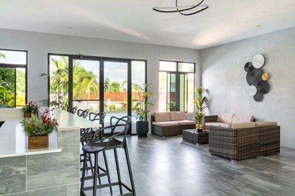 A spacious living area with a large window, a sofa, a dining table with chairs, and a decorative wall piece.