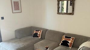 A modern living room with a grey sectional sofa, two wooden stools, and a rustic mirror. - Contemporary villa for 2 people, private pool, enclosed grounds  (San-Gavino-Di-Carbini)