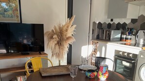 A dining area with a wooden table, chairs, a television, and a kitchen in the background. - Contemporary villa for 2 people, private pool, enclosed grounds  (San-Gavino-Di-Carbini)