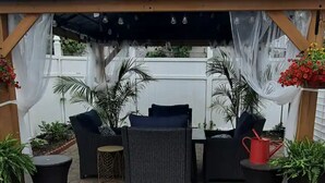 Un espace extérieur aménagé, abrité et doté de mobilier en osier et de plantes en pot.