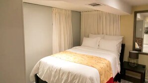 Un lit bien fait, avec une literie blanche et jaune, une table de chevet avec une lampe et un miroir accroché au mur.