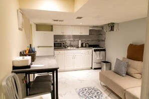 Een knus woongedeelte met een kitchenette, een bank, een eettafel en een vloerkleed met dessin.