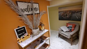 Un espace d’accueil avec une pancarte « Bienvenue », une pancarte « Merci », une pancarte « Bonjour », une pancarte « Que cette maison soit bénie » et un tableau encadré représentant un paysage urbain.
