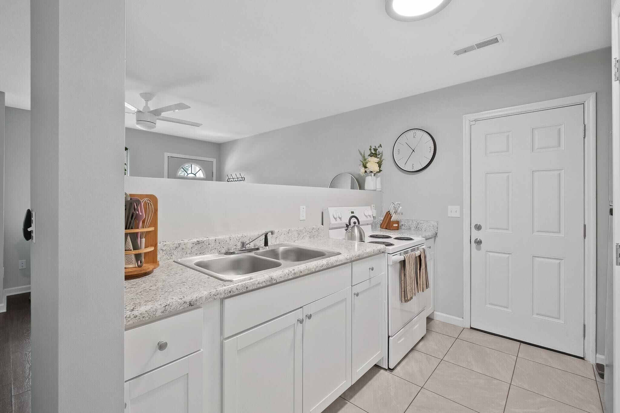 A modern kitchen with white cabinetry, a double sink, a stove, and a clock on the wall.