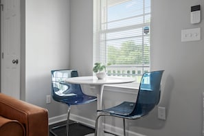 A room with a white table, two blue chairs, a potted plant, a window with blinds, and a door. - Nov Dates Open-Pet friendly near Chatt hospital (Chattanooga)